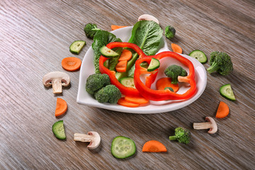 Useful cut vegetables on a plate in the form of heart on wooden table top view