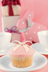 Tasty cupcake with gifts and decorations on pink background