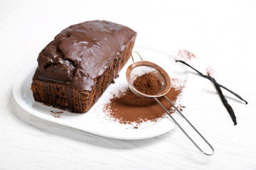 Chocolate cake with icing, cocoa powder and vanilla pods on white table