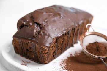 Chocolate cake with icing and cocoa powder on white table