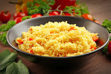 Stewed rice with a carrot on a black plate over wooden background, close up