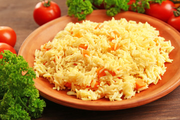 Stewed rice with a carrot on a brown plate over wooden background, close up