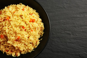 Stewed rice with a carrot on a plate over black background, close up