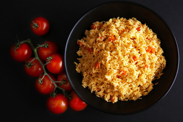 Stewed rice with a carrot and tomatoes on a plate over black background, close up