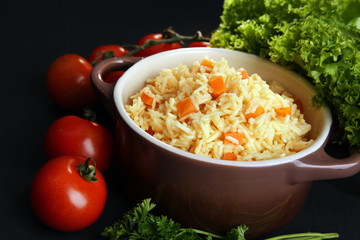 Stewed rice with a carrot and tomatoes in a cooking pot over black background, close up