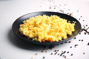 Stewed rice with a carrot on a black plate over white background