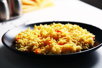 Stewed rice with a carrot on a black plate, close up