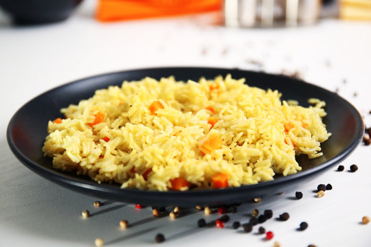Stewed rice with a carrot on a black plate over white background, close up