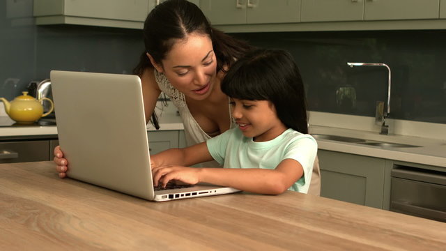 Happy mother and daughter using laptop in the kitchen