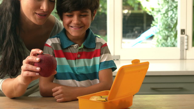 happy mother putting apple in her sons lunch box