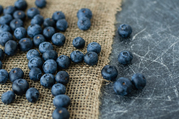 Scattered blueberries on jute tablecloth and scratched black background