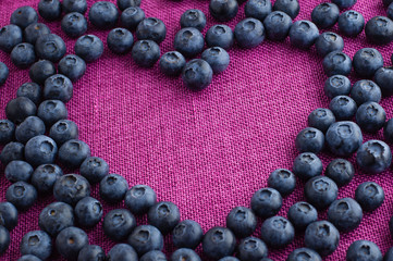 Heart shaped blueberries scattered on a pink jute tablecloth