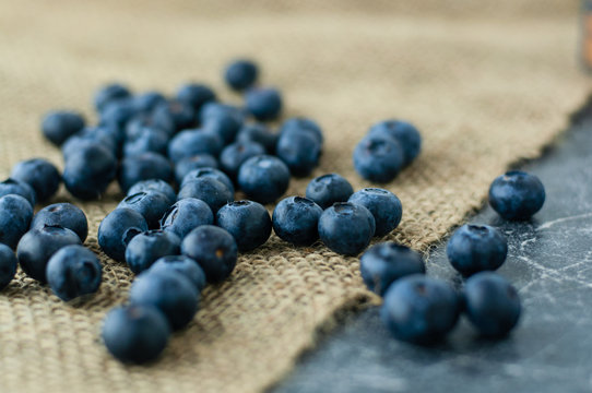 Scattered blueberries on jute tablecloth and scratched black background close up