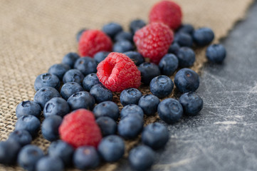 Blueberries and raspberries scattered on a jute cloth and chalkboard background