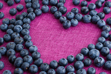 Heart shaped blueberries scattered on a pink jute tablecloth