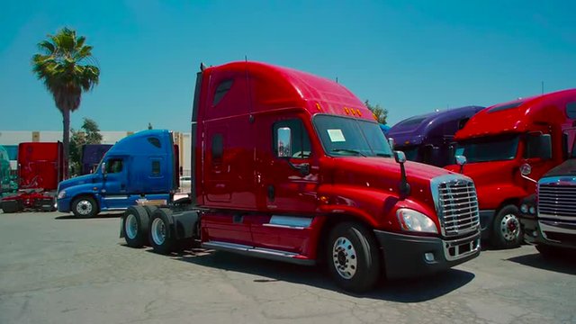 Slow pan down of red freight liner truck parked in an outdoor lot