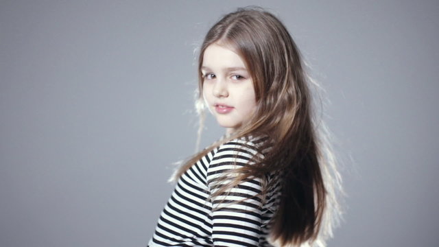 Portrait of beautiful child girl model with long hair posing in studio. Beautiful eight years old girl laughing over grey background.