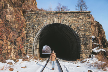 girl is standing back on the rail in front of the tunnel in the rock, in the winter