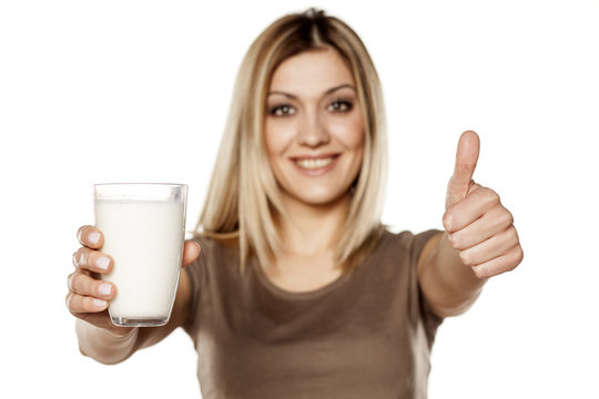 happy young woman holding a glass of milk and showing thumbs up