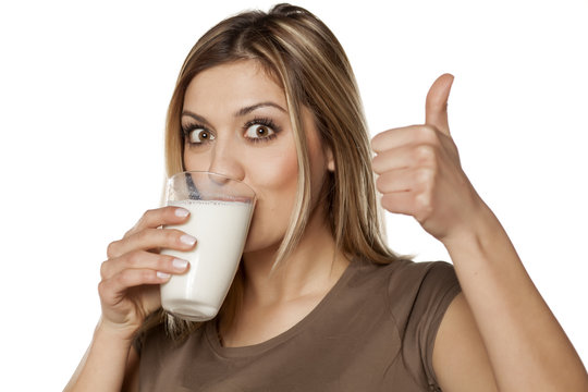 happy young woman drinking milk from a glass and showing thumbs up