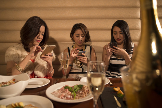 Three women are using a smartphone during a meal in the restaurant