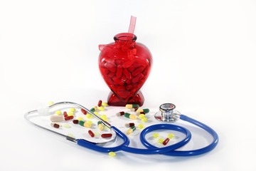 Heart disease. Red Heart shaped bottle filled with drugs/pills/tablets  and blue stethoscope on a blue background