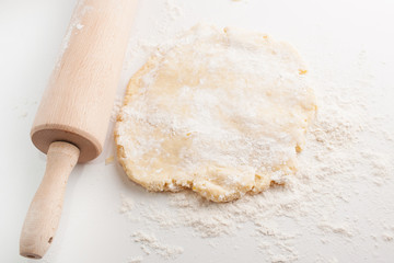 Block of freshly made pastry rolled out on a floured work surface with a wooden rolling pin