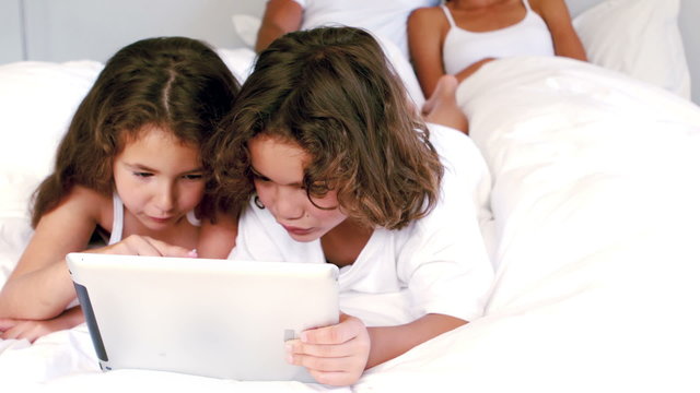 Cute siblings using tablet on their parents bed