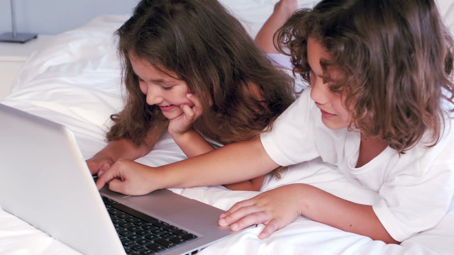 Cute siblings using laptop on their parents bed