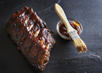 half rack of baby back barbecued pork ribs on slate with sauce brush