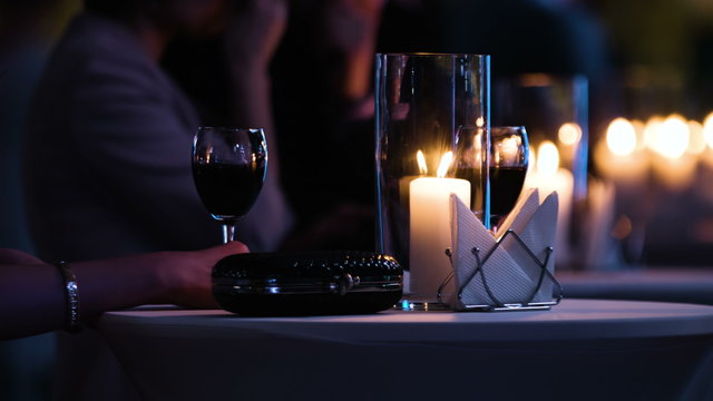 Close-up footage of elegantly decorated table at restaurant,female visitor holding a glass of red wine, fancy black clutch bag is near. 