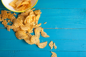 Potato chips poured out of the plate on a blue wooden table