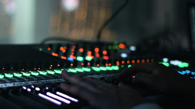 Close-up picture of male hands put on a sound control desk. Audio engineer operates his instrument, recording equipment, during a night show at concert hall.  