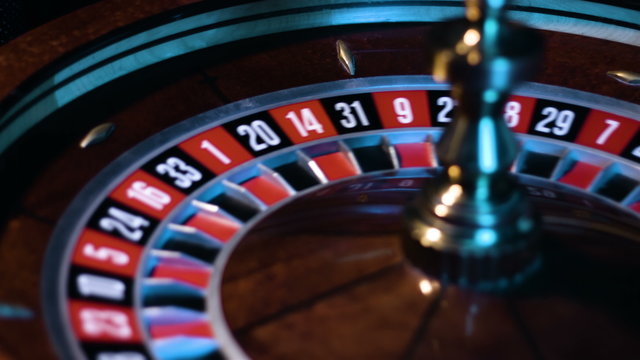 Russian roulette wheel is spinning with the small white ball is going around at the game table at casino. 