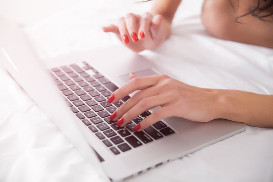 Woman hands with laptop computer on the bed