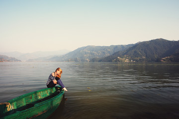 Young Woman sitting on boat at mountain Lake. Calm and quiet landscape. Relax outdoor