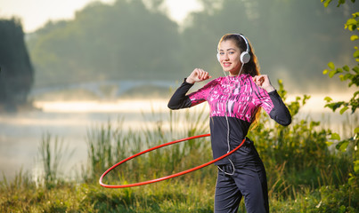 young woman doing hula hoop outdoors near the lake - obrazy, fototapety, plakaty