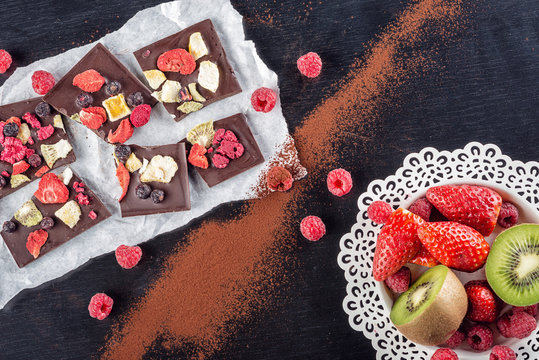 Sweet chocolate slices with fruits, cocoa powder on paper and fruit on metal white plate. sweet dessert on black background, image for patisserie 