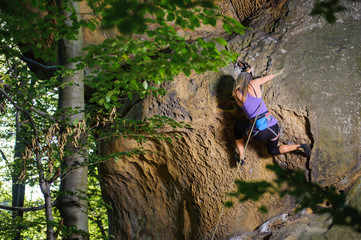 Female rock climber on her challenging way up, bouldering. Summer time. View from the back.