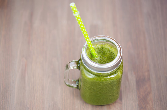 A green smoothie in a mason jar with tube on wooden background