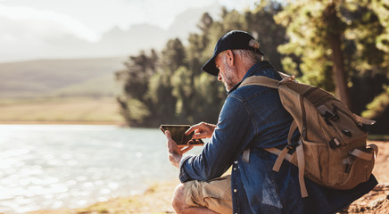 Mature man on hike in nature using digital tablet
