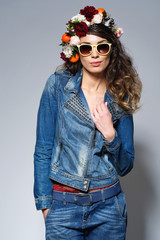 Fashion portrait of a beautiful young woman with gypsy hairstyle wearing bright flower crown, jeans jacket and trendy yellow sunglasses