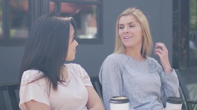 Two friends sitting on a bench in a city and talking
