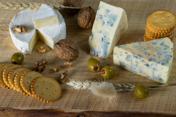 camembert and blue cheese with green olives and crackers on the wooden board as a perfect appetizer