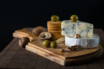 camembert and blue cheese with green olives and crackers on the wooden board as a perfect appetizer