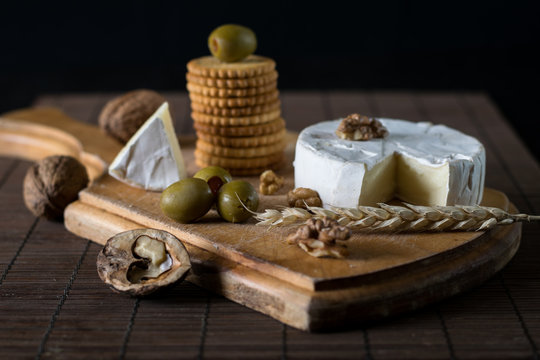 camembert and blue cheese with green olives and crackers on the wooden board as a perfect appetizer