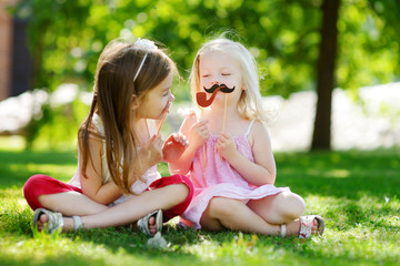 Adorable little girls playing with paper moustaches on a stick and other accessories