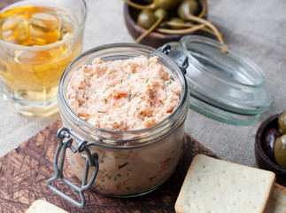 Smoked salmon and soft cheese spread, mousse, pate in a jar with crackers and capers on a wooden background