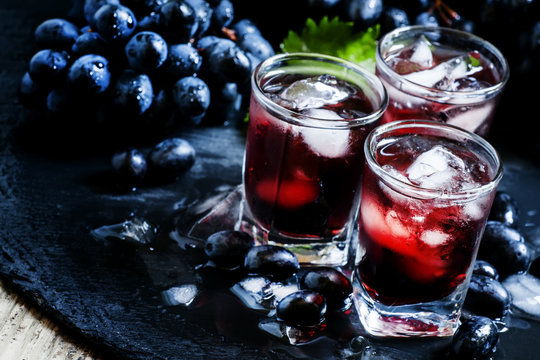 Cold juice of black grapes with ice on a dark background, select