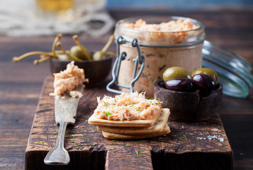 Smoked salmon and soft cheese spread, mousse, pate in a jar with crackers and capers on a wooden background